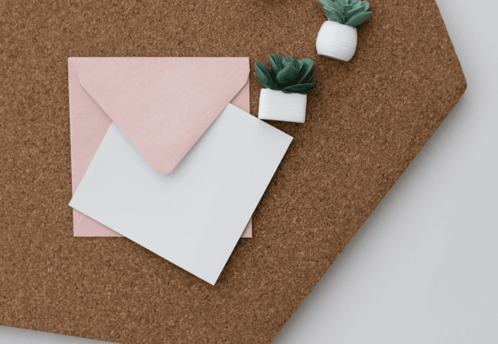 pink envelope and piece of paper on a desk next to plants. where to buy stamps near me and online